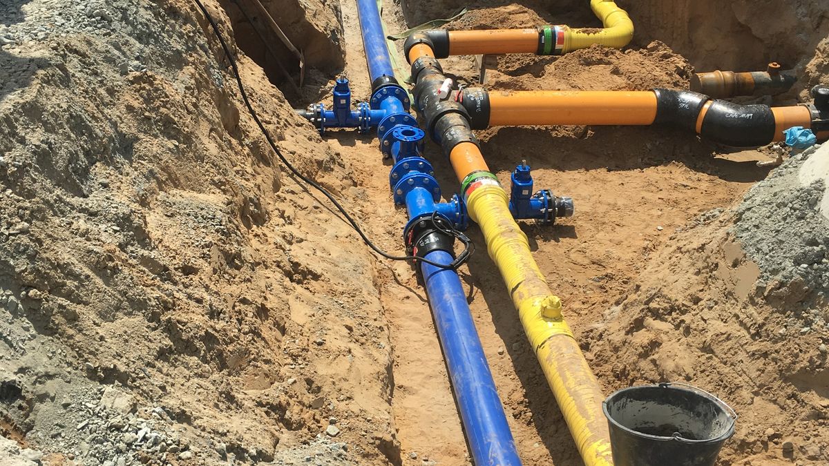 Offener Leitungsgraben mit blauen Wasser- und gelben Gasleitungen auf einer Baustelle