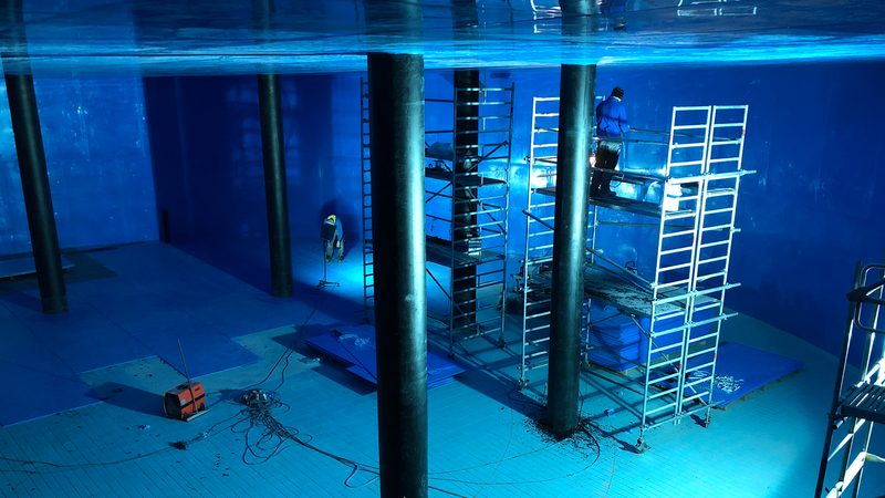 Blau gestrichene Kammer eines Wasserhochbehälters, in der zwei Arbeiter auf Gerüsten die Wände sanieren